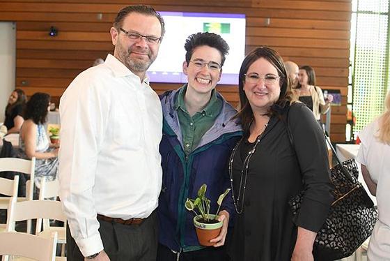 A graduating Falk student holding a plant poses with their family on Eden Hall Campus